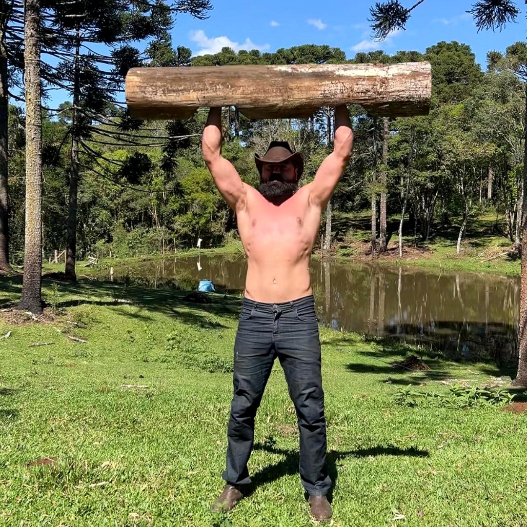 Homem levantando um tronco no campo